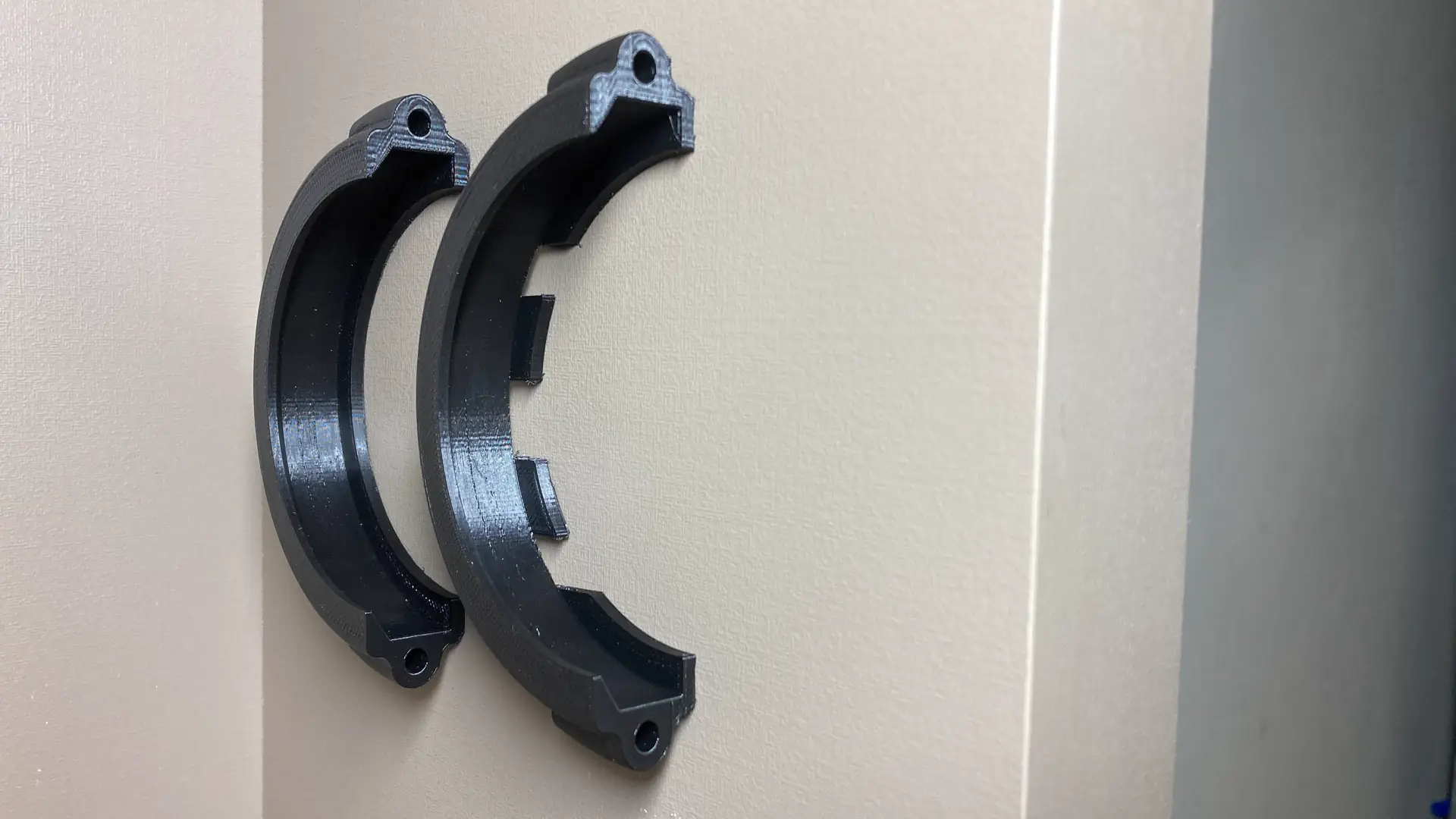 Duas metades de uma braçadeira preta impressa em 3D, dispostas em arco sobre superfície clara; a da direita tem recortes internos de encaixe