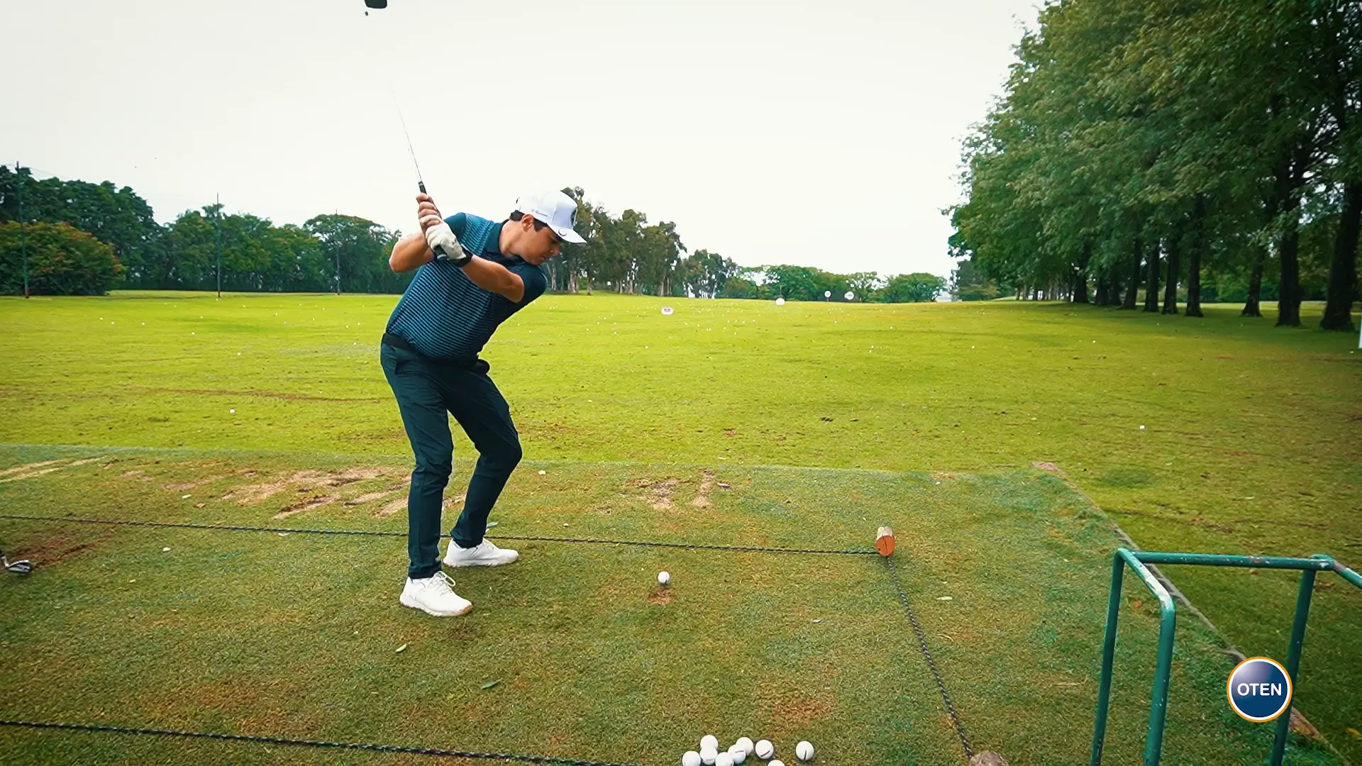 Golfista no momento do swing no campo de treino, sob árvores