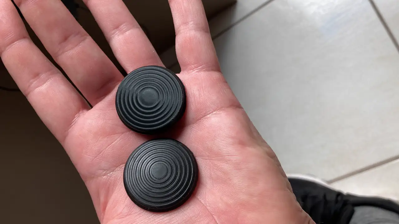 Duas peças pretas circulares com sulcos concêntricos, apoiadas na palma de uma mão